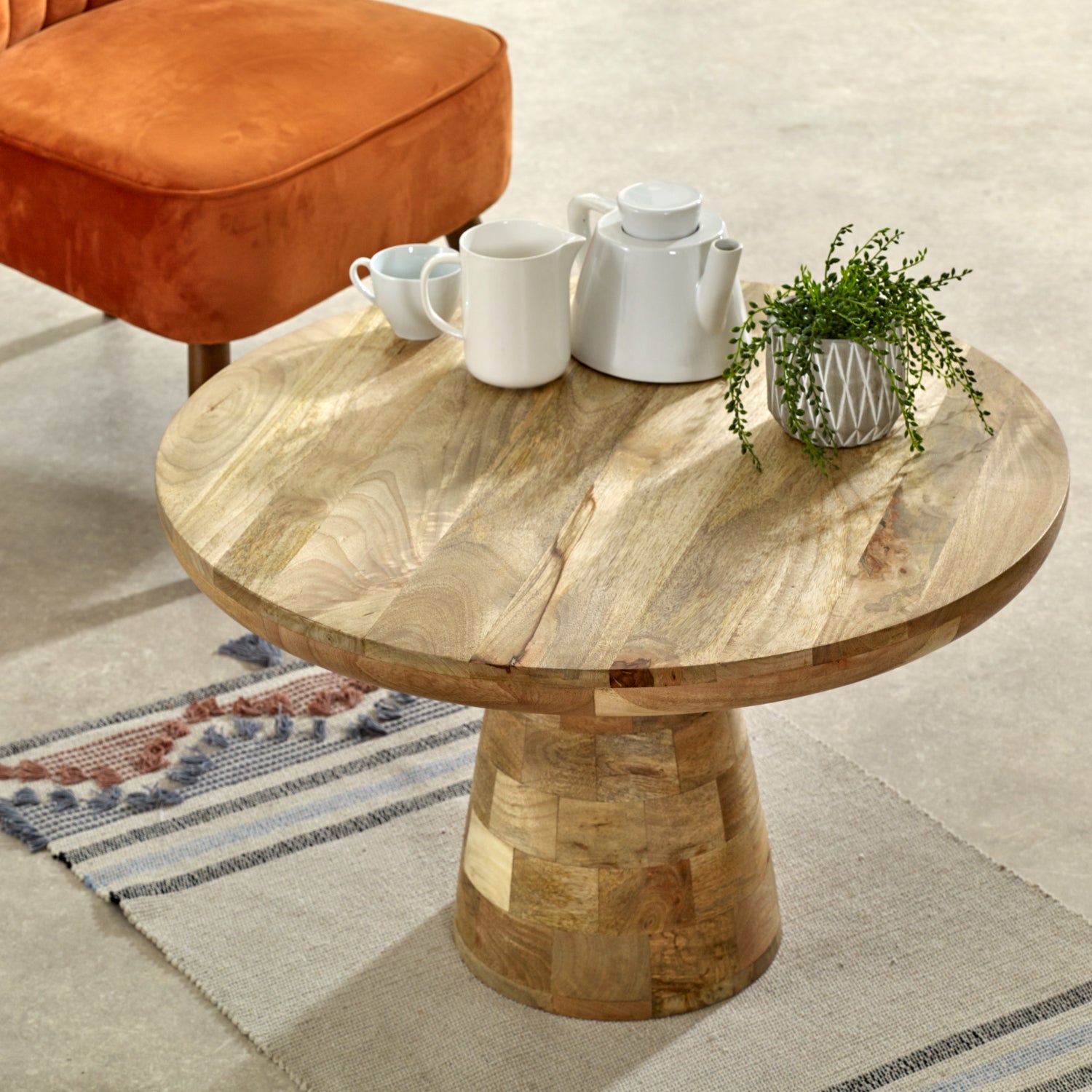 Merlin Mango Wooden Round Coffee Table Mushroom Style Wooden coffee table with white ceramic items and a plant in a living room setting.