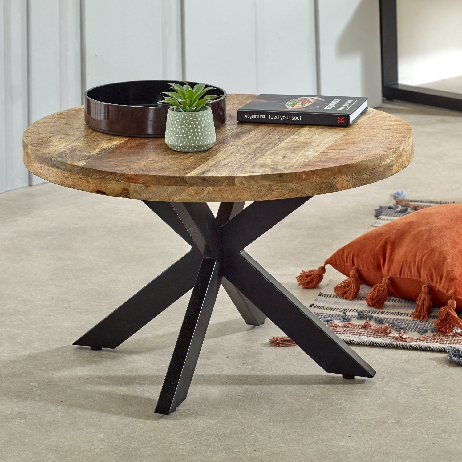 Merlin Mango Wooden Round Coffee Table Spider Legs Round wooden coffee table with black metal legs in a living room setting.
