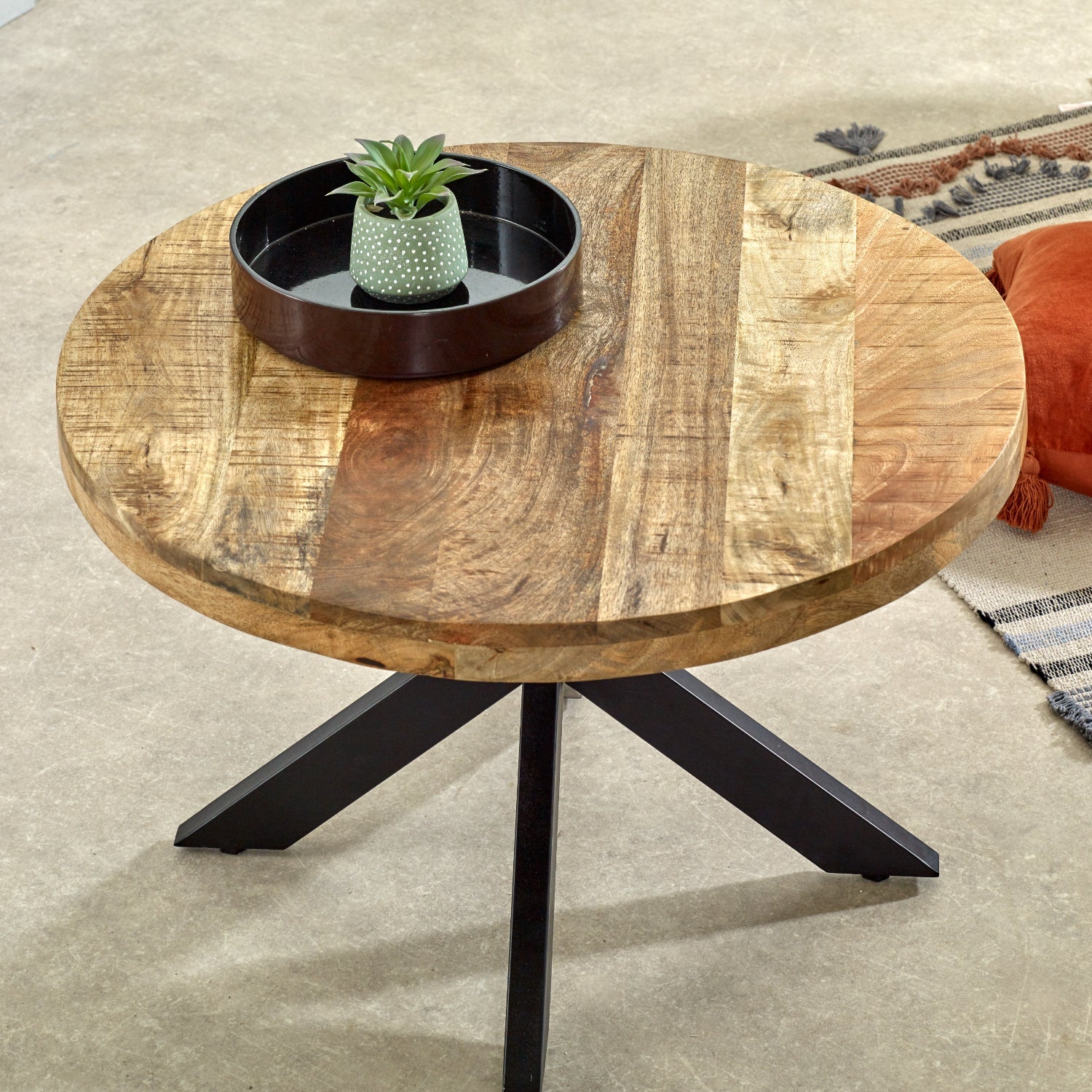 Merlin Mango Wooden Round Coffee Table Spider Legs Round wooden table with black metal legs on a beige carpet