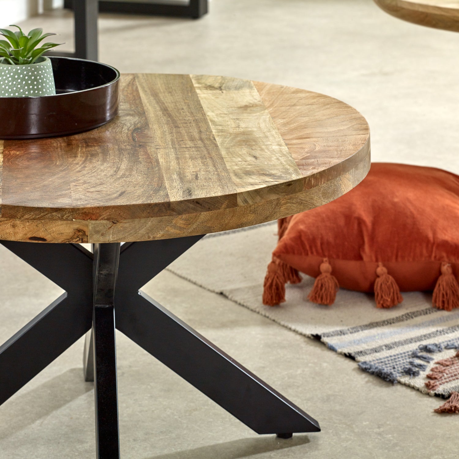 Merlin Mango Wooden Round Coffee Table Spider Legs Wooden coffee table with black metal legs in a living room setting.