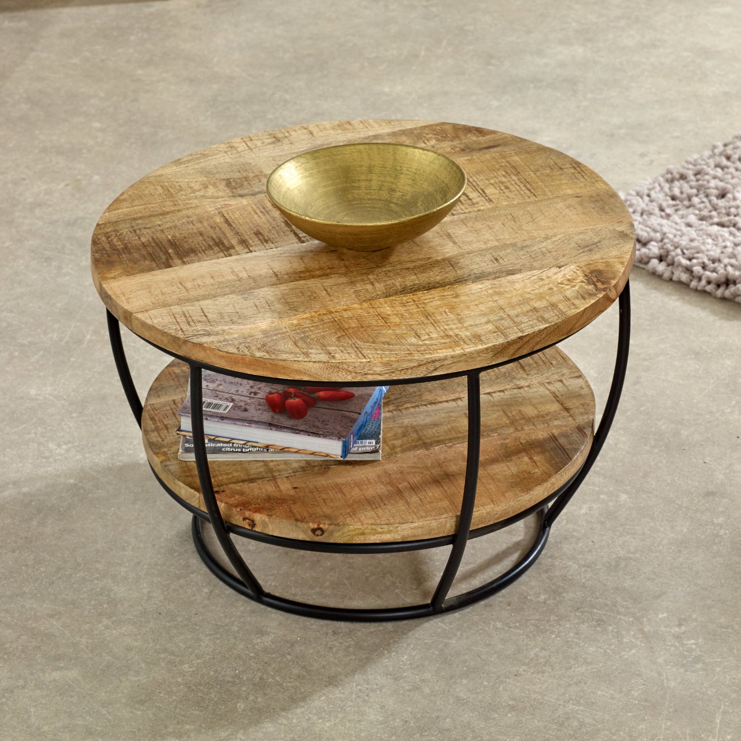 Merlin Mango Wooden & Metal Coffee Table With Shelf Round wooden coffee table with a metal frame on a concrete floor.