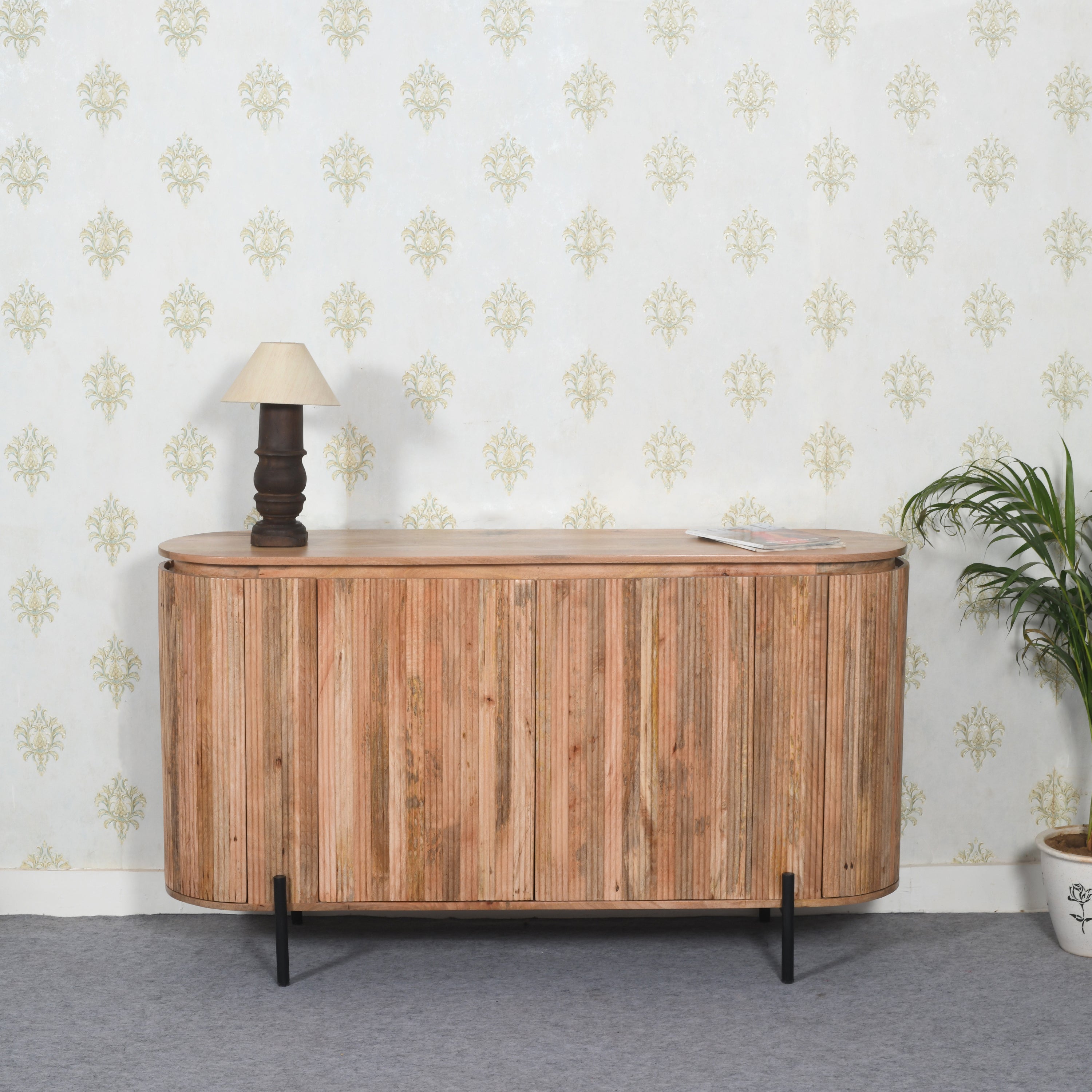 York Solid Wood Sideboard With Metal Legs Wooden sideboard with a lamp and plant against a patterned wall.