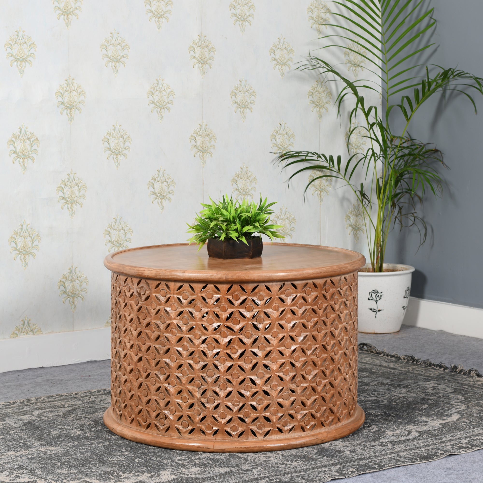 Carved Mango Wood Round Coffee Table Woven wooden side table with plants in a room setting